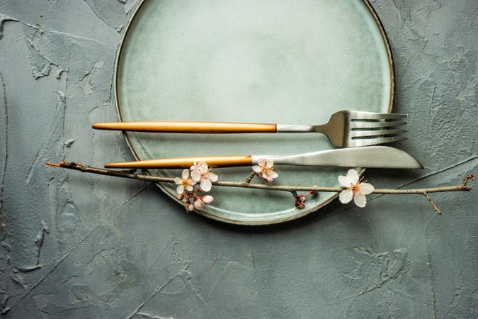 Top view of spring table setting with blooming tree branch on grey plate with cutlery