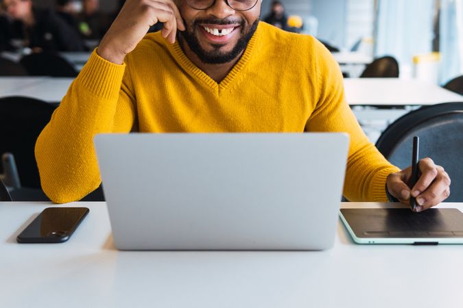Anonymous smiling Black man working on laptop with tablet