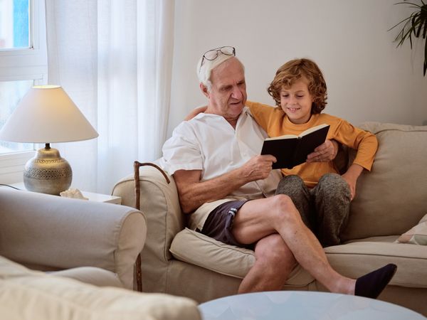 Kid spending time with grandfather while reading book on couch