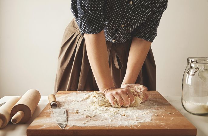 Woman needing lumpy pasta dough on bread board