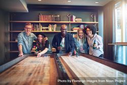 Multi-ethnic group of friends smiling while playing shuffleboard 4jBvR4