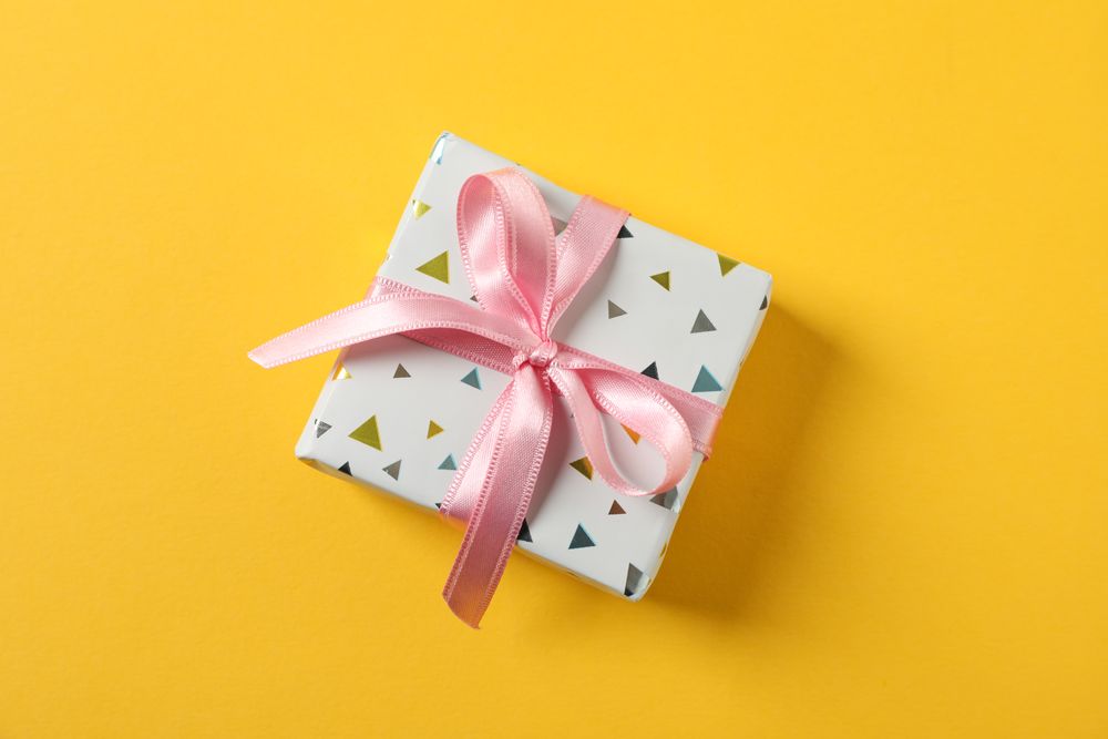 Gift box with bow on yellow background, space for text