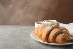 Plate with croissants, cups of coffee and towel on grey table, and brown background, space for text