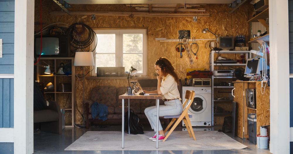 Hispanic Female Software Engineer Programming On Laptop Computer In Garage At Home.