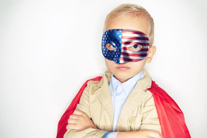 Serious blond boy wearing American flag mask with arms crossed