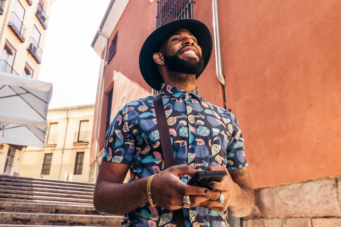 Stylish Black man walking on the city street using smartphone