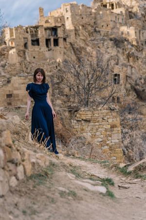 Mature woman in long blue dress standing near Hamsutl abandoned village in Dagestan