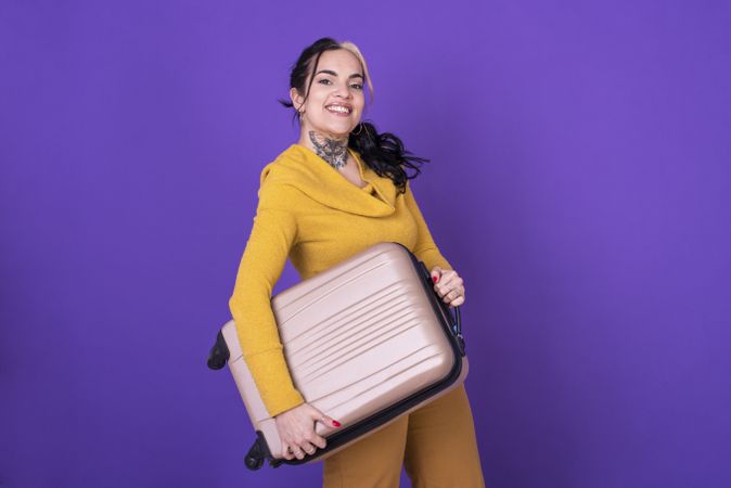 happy woman traveler holding her suitcase against purple background.