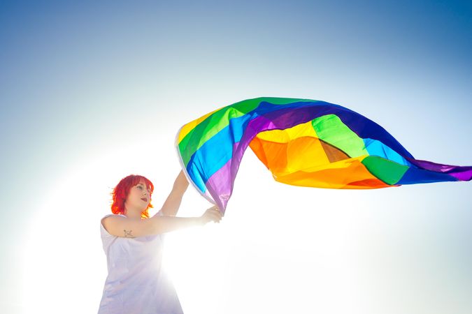 Woman waving rainbow flag under blue sky