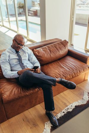 Businessman using mobile phone sitting on a lounge, vertical