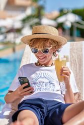 Boy holding drink and using smartphone on sunbed