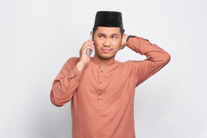 Bored Muslim man in kufi hat talking on smartphone