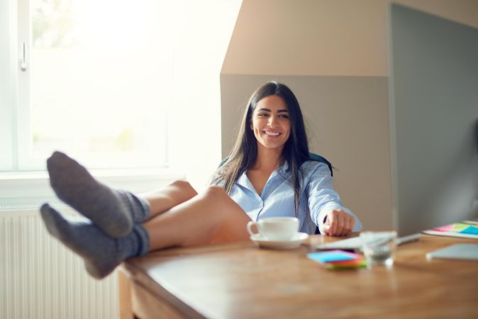 Woman smiling with feet up on desk looking at computer monitor