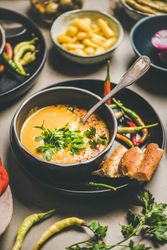 Yellow lentil soup bowl, bread, vegetable garnishes, selective focus, vertical composition