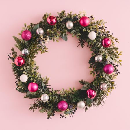 Christmas wreath made of decorative baubles and branches on pink background