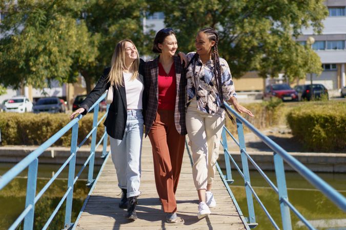 Three smiling women walking over pedestrian bridge on summer’s day