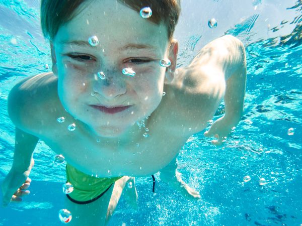 Funny boy swimming underwater looking at camera