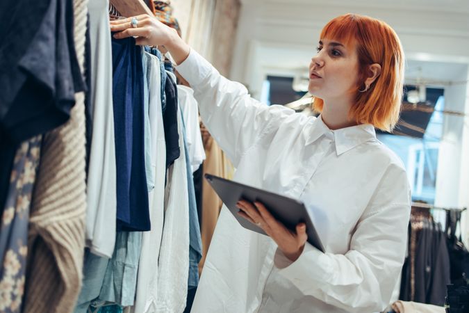 Female manager looking at clothes hanging on rack in store