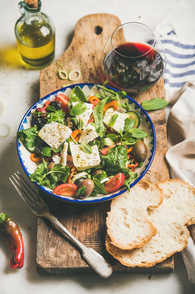 Greek salad with feta, tomatoes, and red wine on wooden board, vertical composition, selective focus