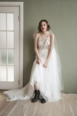 Adult confident female in white dress and military shoes leaning on wall