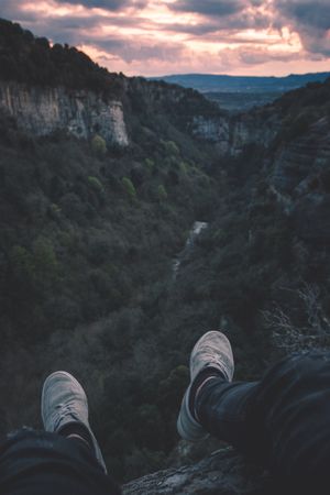 View to small river in canyon and legs of person sitting on the edge
