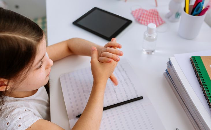 Girl applying hand sanitizer while doing homework