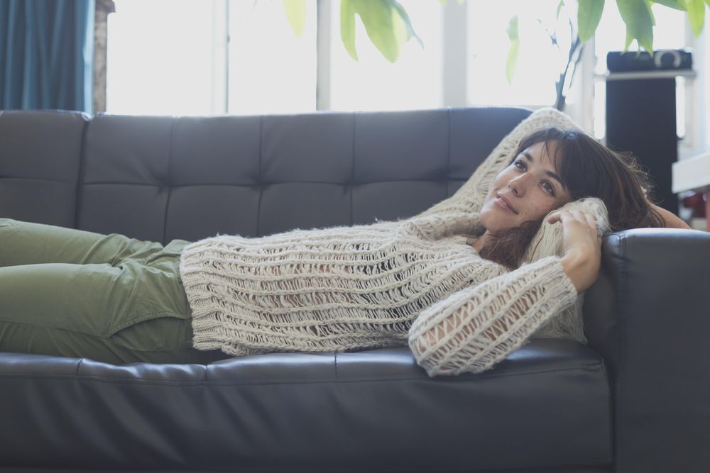 Female in wooly sweater lying on leather couch in living room