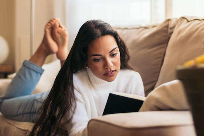 Relaxing at Home: Young Woman Reading a Book on the Sofa