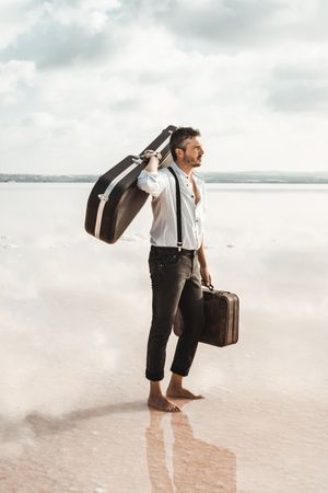 Focused stylish man with suitcase and guitar gig bag on seaside
