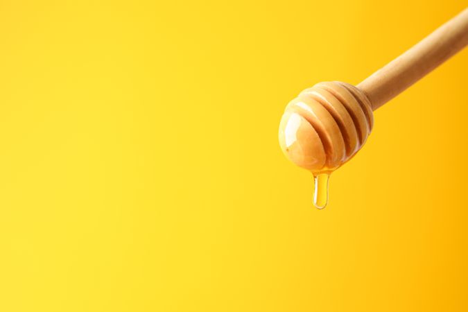 Dipper with honey on yellow background, space for text