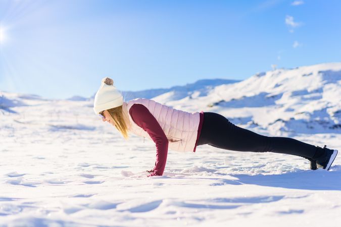 Side view of female in snowsuit doing plank on snowy mountain