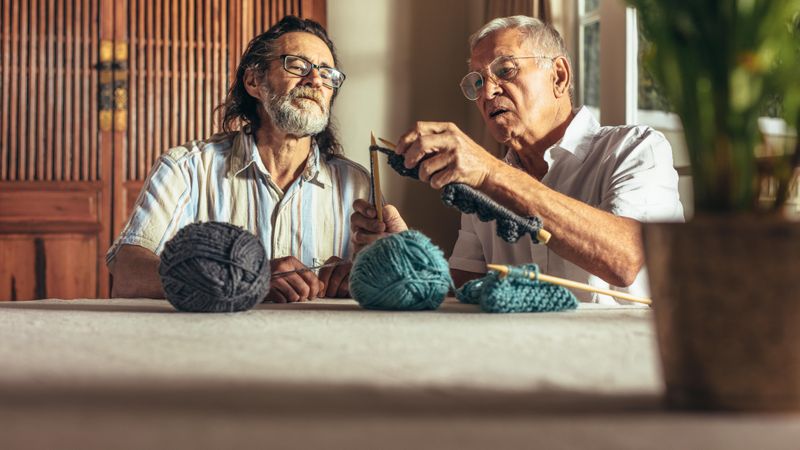 Older man teaching his friends the art of knitting woolen clothes