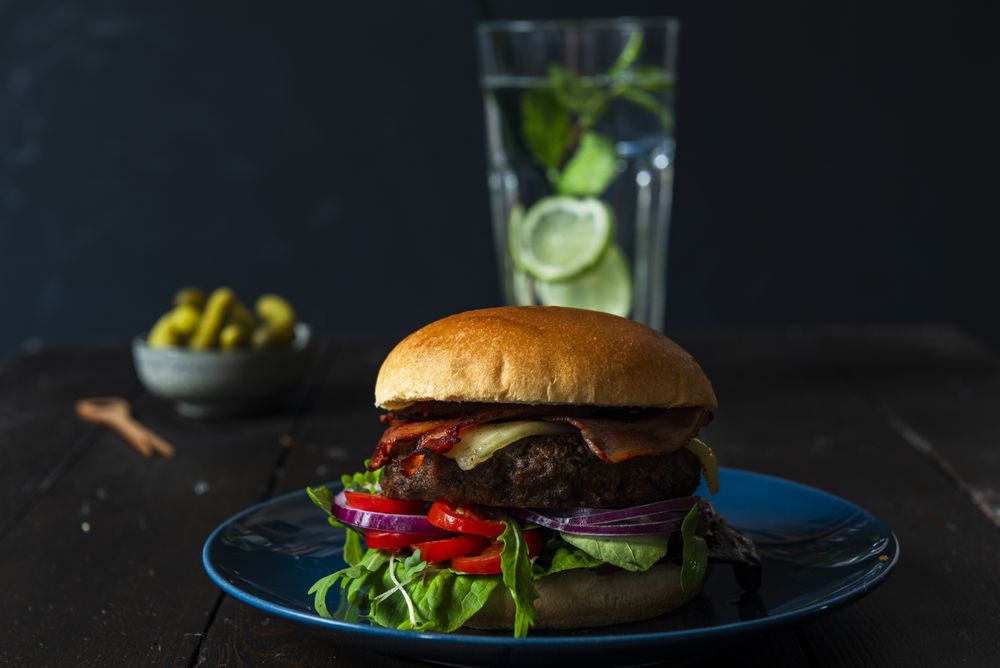 Burger on a blue plate water and pickels in the back