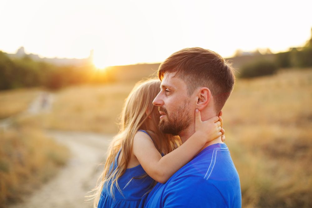 Man carrying daughter in long grass meadow at meadow