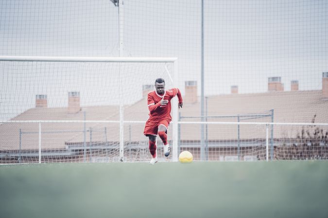 Black soccer player with red outfit playing soccer.