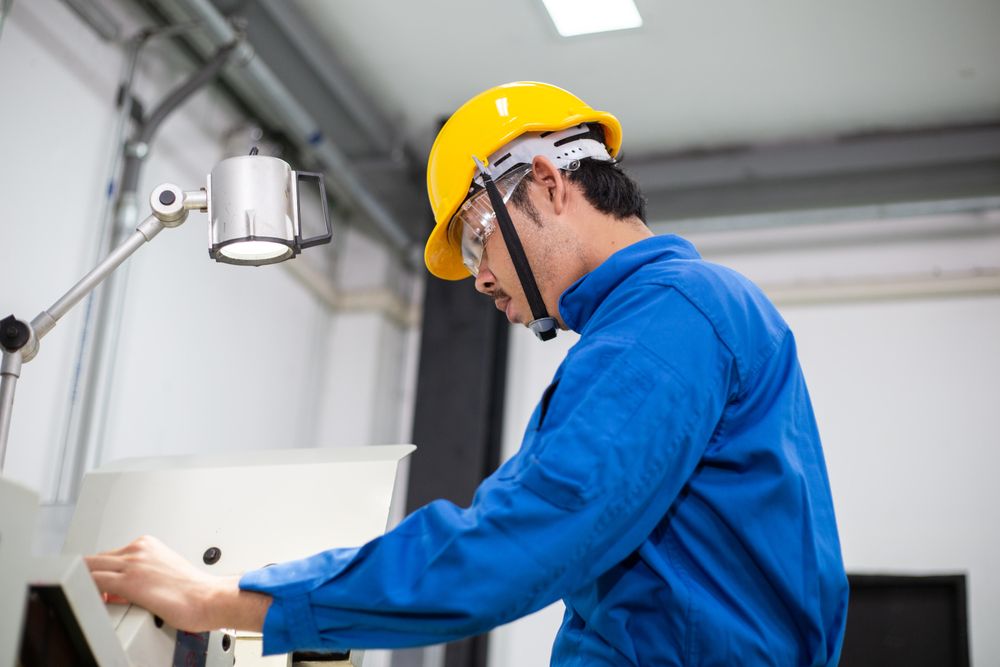 Asian man in blue jumpsuit and yellow hard hat working with machinery