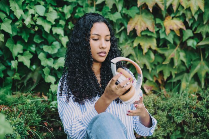 A young woman enjoys music with headphones, sitting peacefully amid vibrant green nature