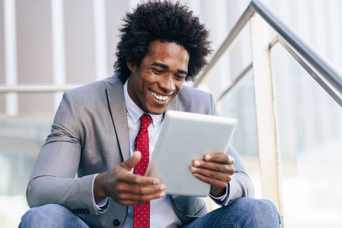 Laughing man sitting on stairs with digital tablet