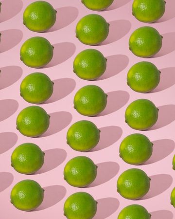 Rows of fresh limes on pink background with shadow