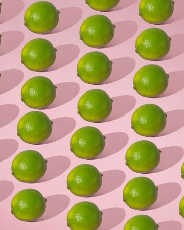 Rows of fresh limes on pink background with shadow
