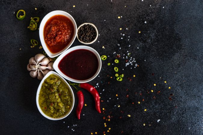 Top view of three flavorful spicy traditional Georgian sauces on dark counter with garlic & chilis