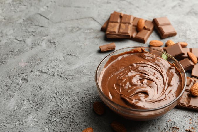 Bowl with chocolate and chocolate pieces on gray background