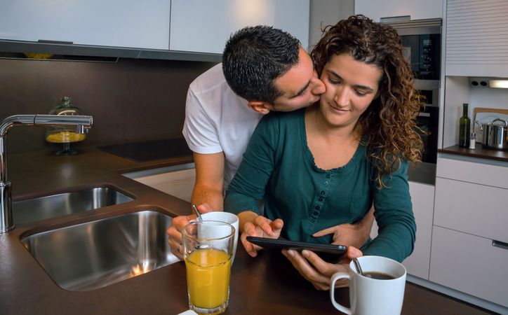 Affectionate couple reading digital table in kitchen at breakfast time