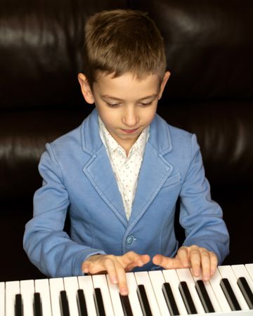 Young boy in blue blazer playing piano with focus.