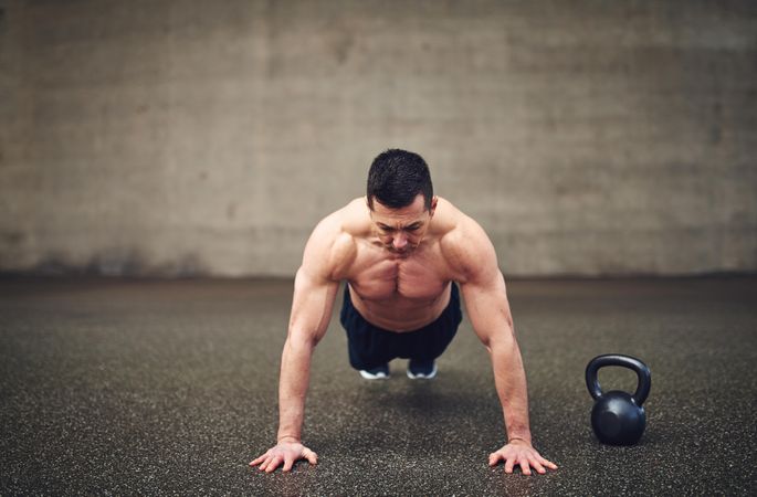 Man doing planks in concrete space next to weight