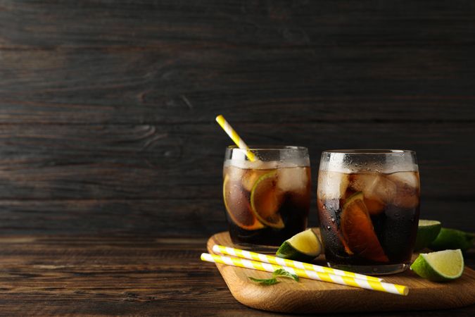 Glasses with ice cola, lime slices and tubules on wooden background