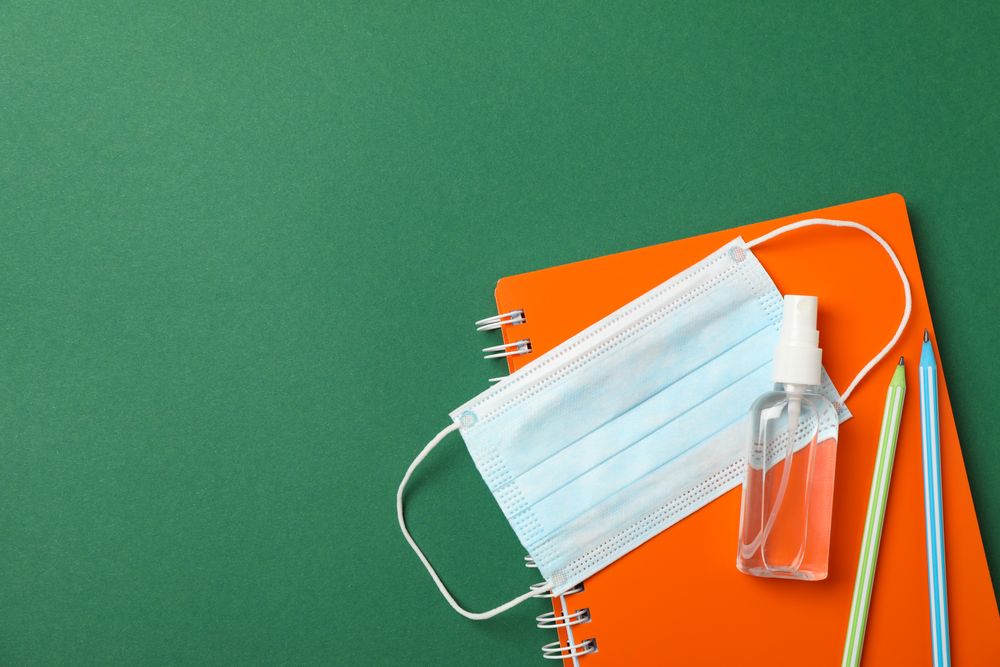 Medical mask, sanitizer, notebook and pencils on green background