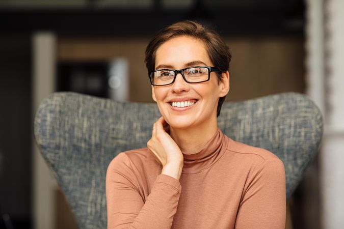 Portrait of happy woman with short hair and eyeglasses sitting in smart casual