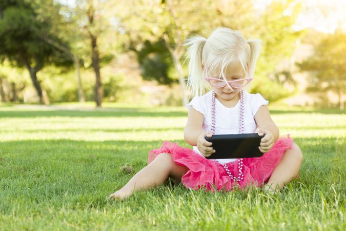 Little Girl In Grass Playing With Cell Phone