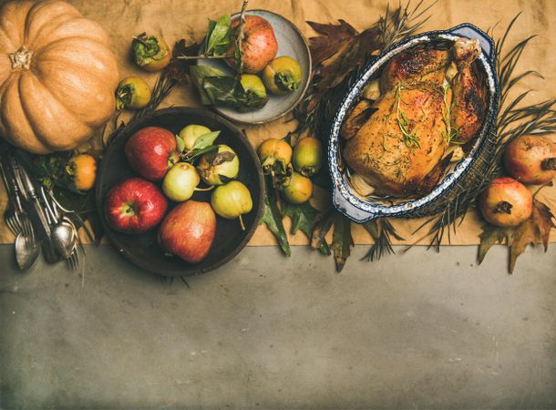 Roast turkey in roasting pan, on concrete table with leaves and fruit, copy space